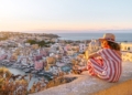 Side view of positive mature female traveler in striped dress and hat enjoying amazing seascape during sunset in Procida island.